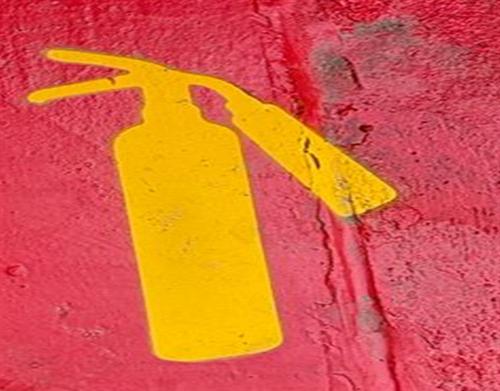 Ícono de extintor pintado en amarillo sobre superficie roja
